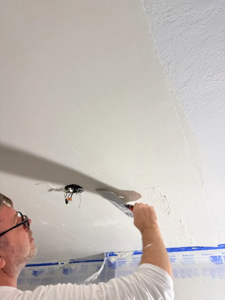 Applying joint compound to level the ceiling and create a flat surface.